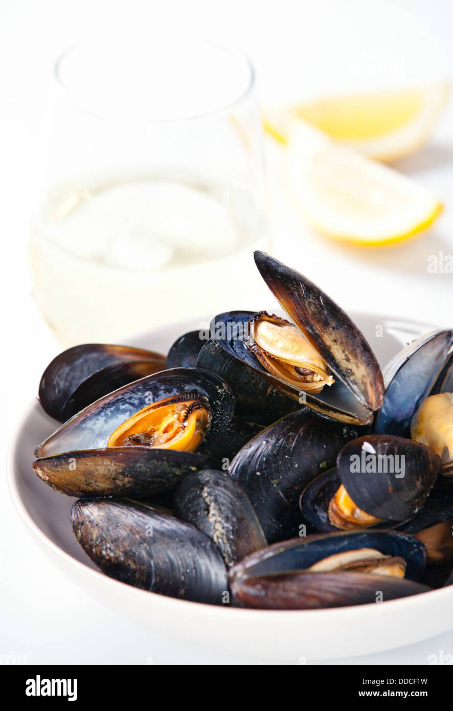 Mussels and clams served in white bowl with glasses of white wine and piece of lemon Stock Photo