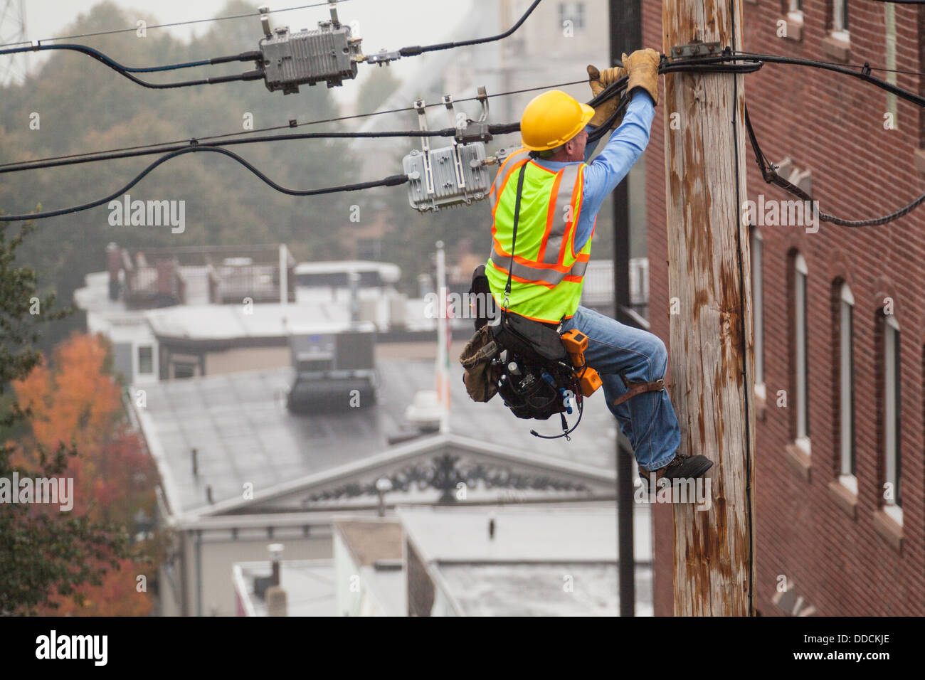 Cable lineman holding onto pole while using lineman spikes to adjust