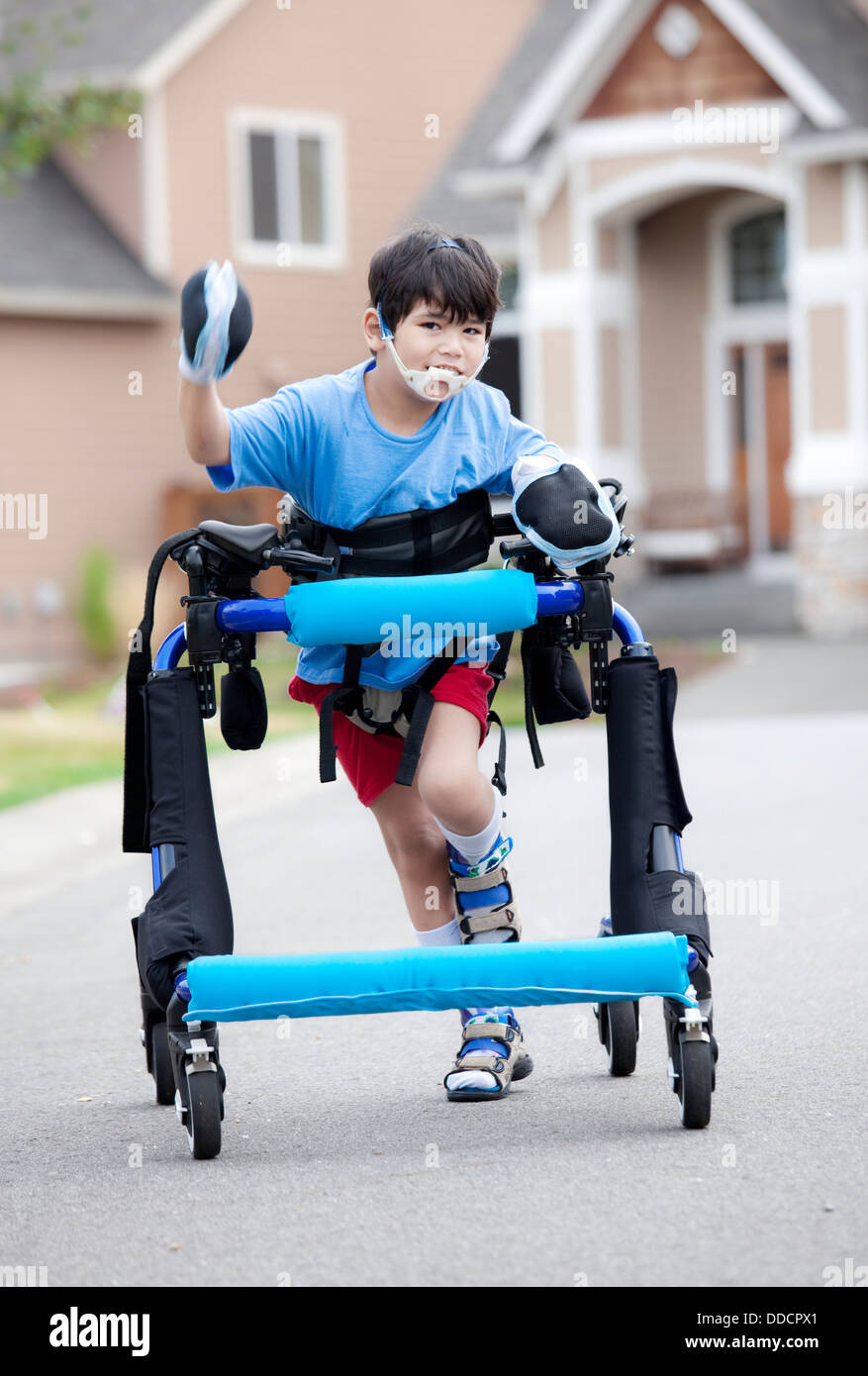 Six year old disabled boy walking in walker down the street Stock Photo
