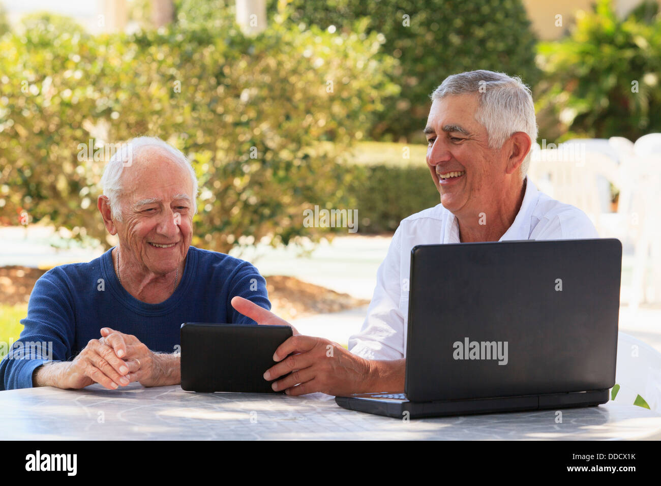 Senior man smiling showing a digital tablet to his father Stock Photo