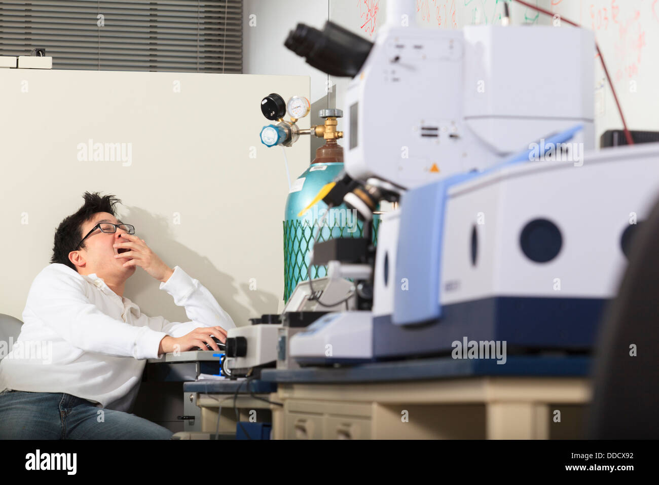 Engineering student using keyboard for chemical analysis instrument and yawning in a laboratory Stock Photo