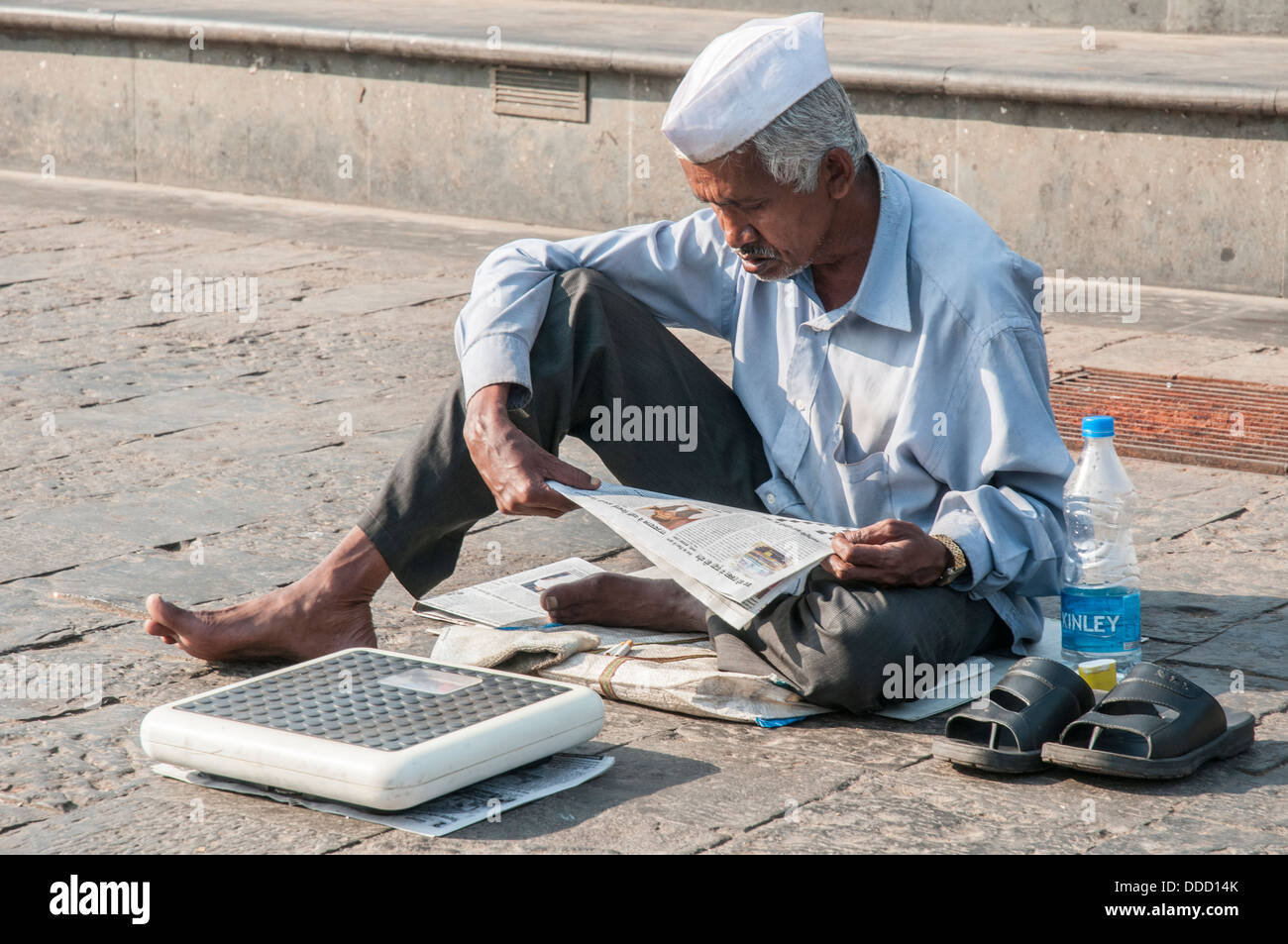 Man offering scales for weighing awaits customers near the Haji Ali Mosque, Mumbai, India Stock Photo