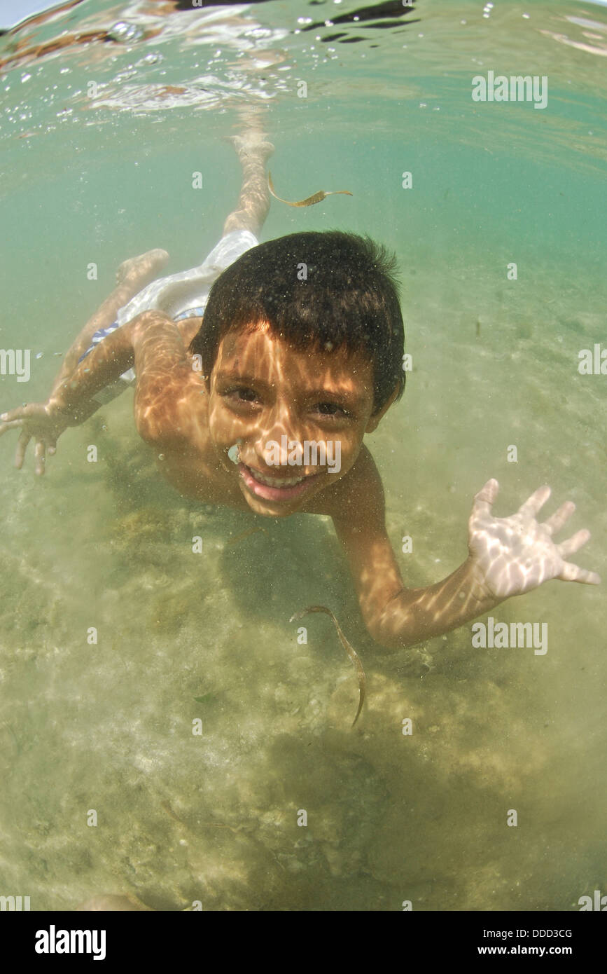 A young boy smiles into the camera as he swims in the Caribbean. Stock Photo