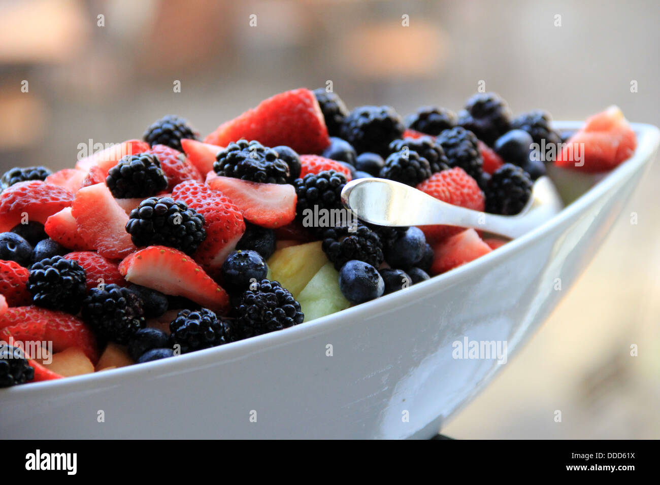 Scrumptious breakfast of seasonal fresh berries and melons in white bowl with serving spoon is a must for health conscious eater Stock Photo