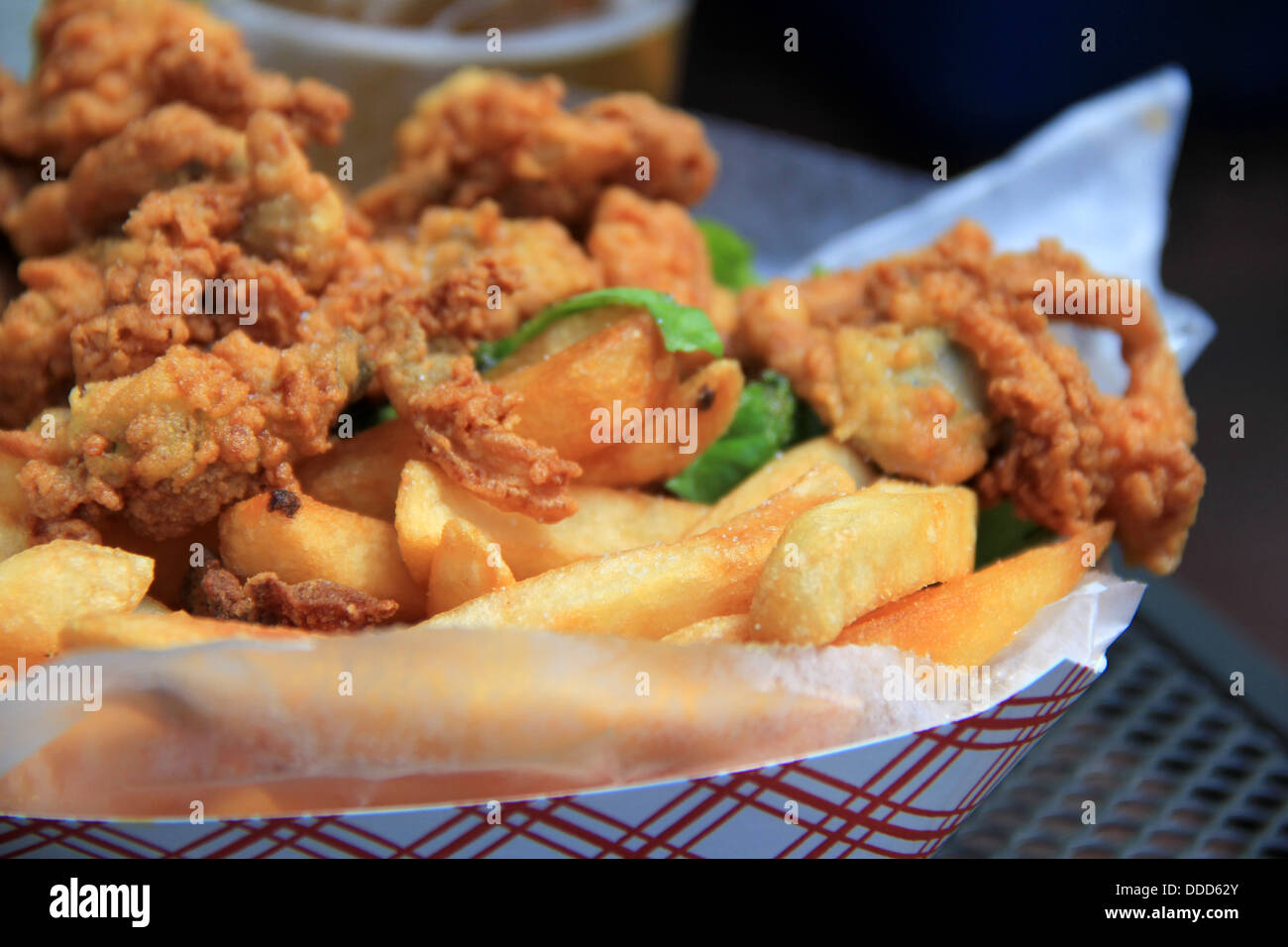 Golden fried whole belly clams with crispy French fried potatoes on wax paper in basket on table at outdoor seafood restaurant. Stock Photo