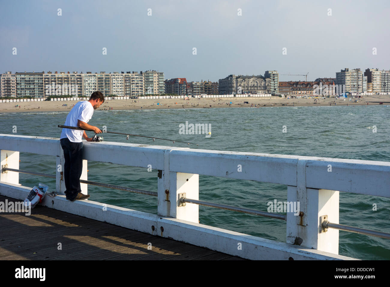 Angler fishing with fishing rod from pier along the North Sea coast at Nieuwpoort / Nieuport, Belgium Stock Photo