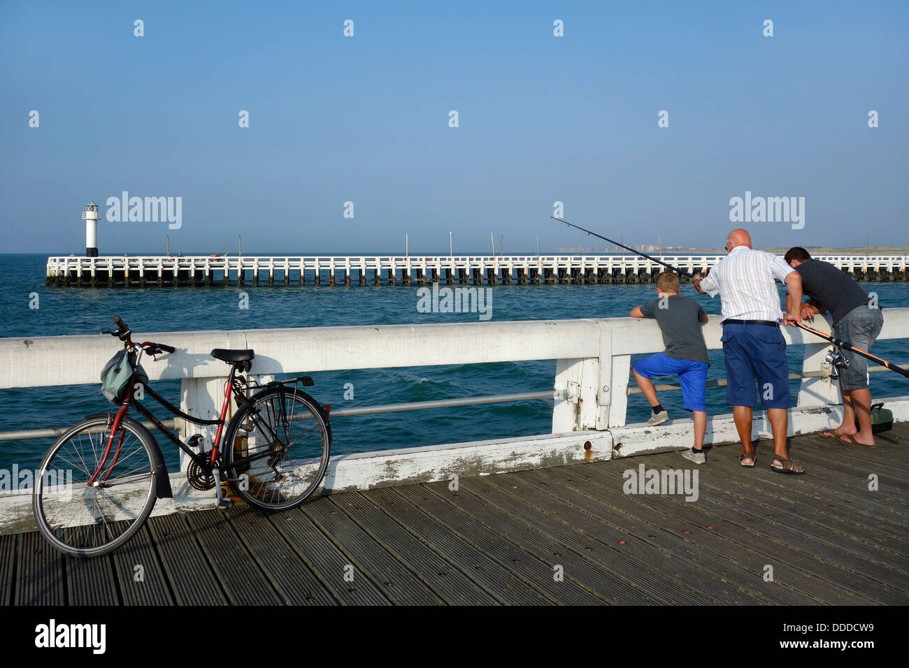 Son, father and grandfather angling with fishing rod from pier along the North Sea coast at Nieuwpoort / Nieuport, Belgium Stock Photo