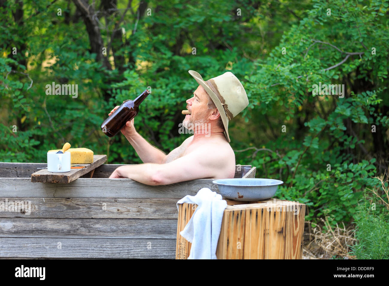 A Cowboy taking a drink from his whiskey bottle while bathing and shaving Stock Photo