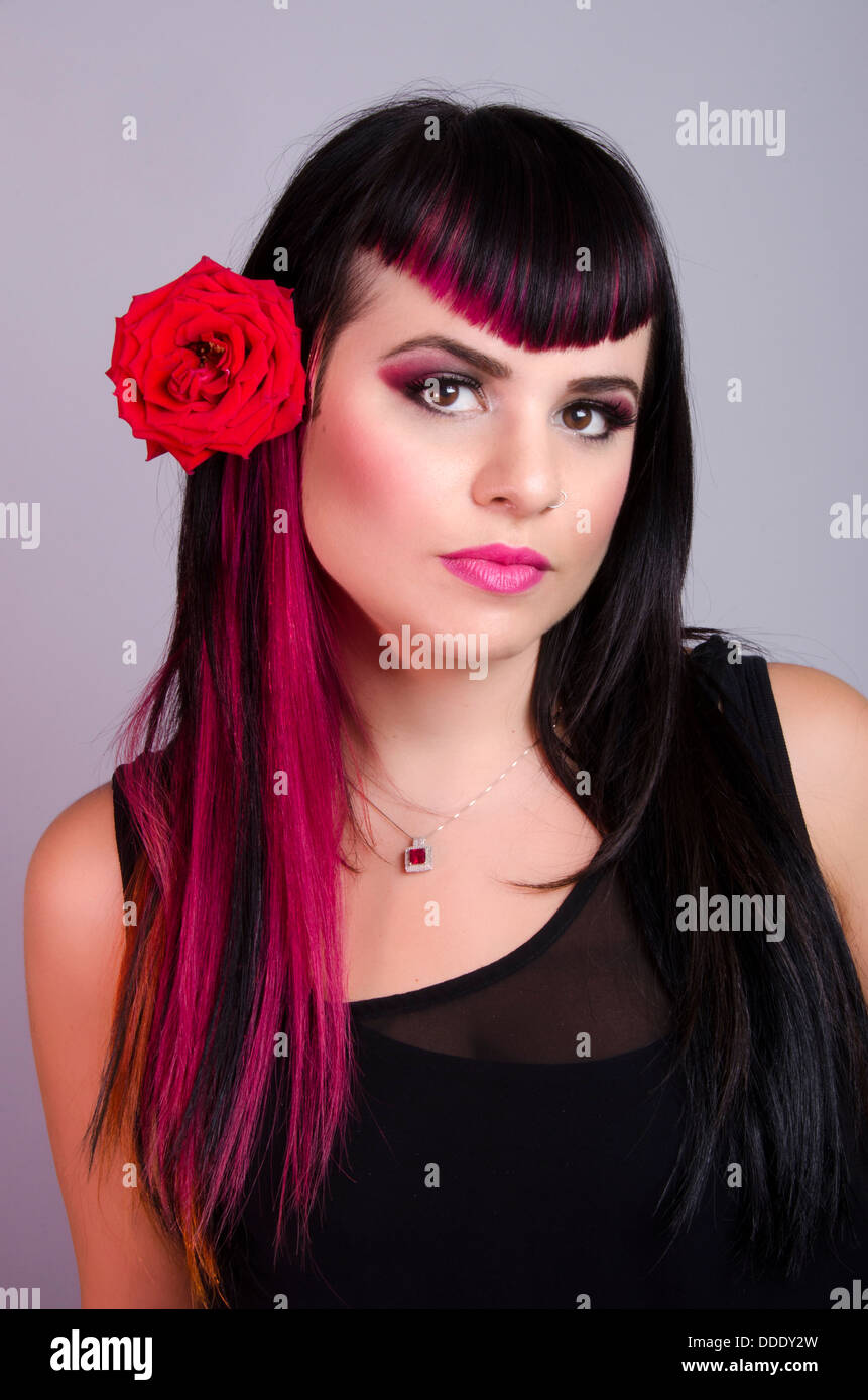A young scene/goth model with a bangs and pink extensions, with a rose in her hair, in a studio setting Stock Photo
