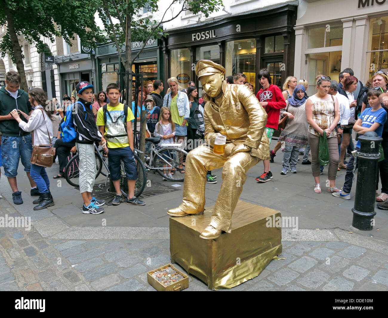 Street performer busker dressed in gold sitting on an invisible chair in Covent Garden, London Stock Photo