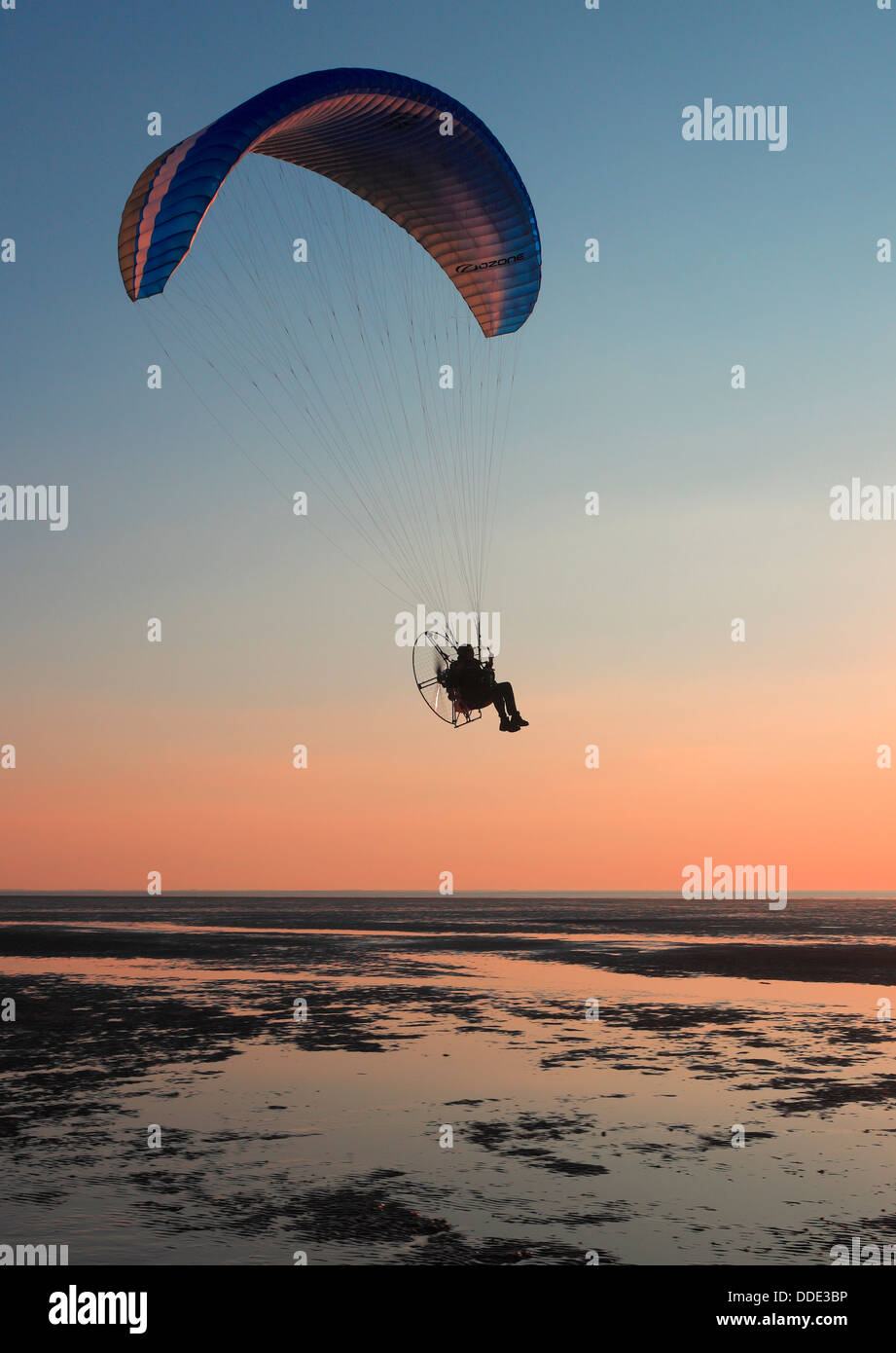 Man in a powered paraglider over Heacham beech with the sun setting over The Wash. Stock Photo