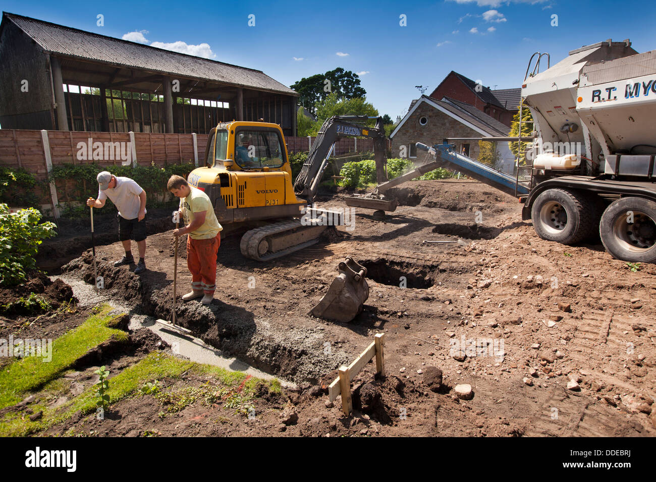 self building house, tamping concrete foundations after being poured using bucket of volvo digger Stock Photo