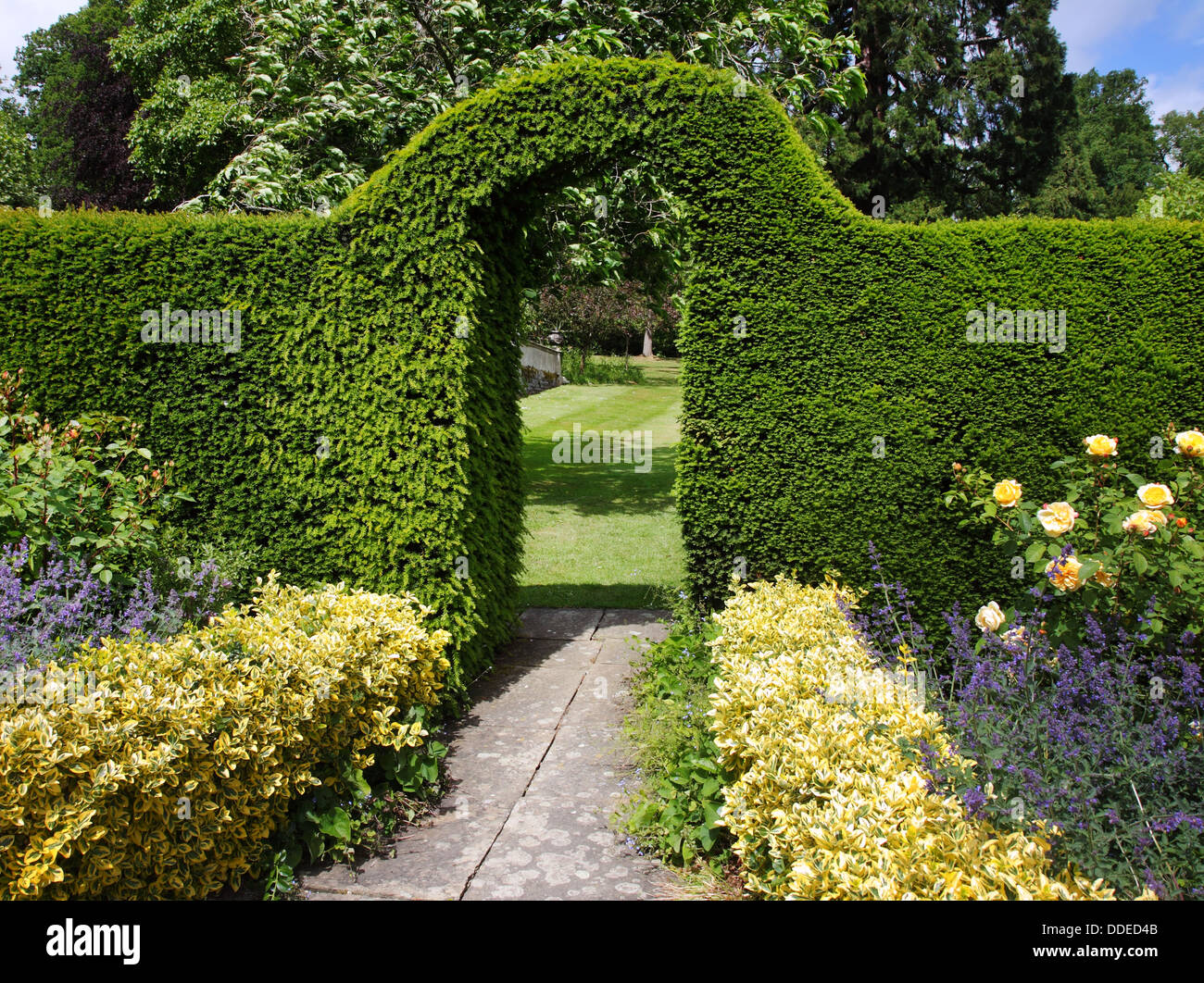 An English Landscape Garden in early Summer with flowerbeds and an Arch through a Hedgerow Stock Photo