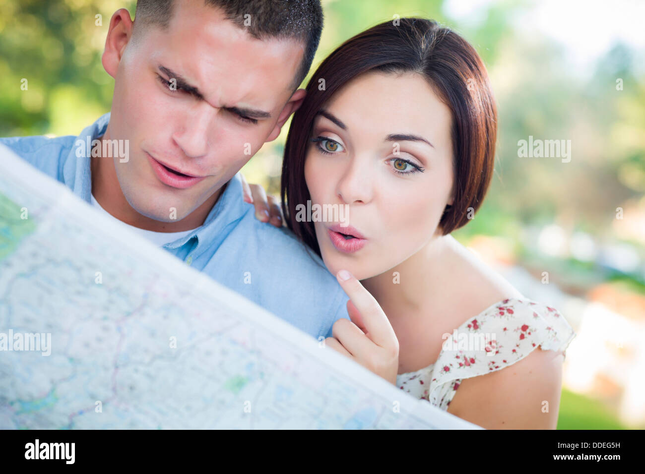 Happy Mixed Race Couple Looking Over A Map Outside Together. Stock Photo