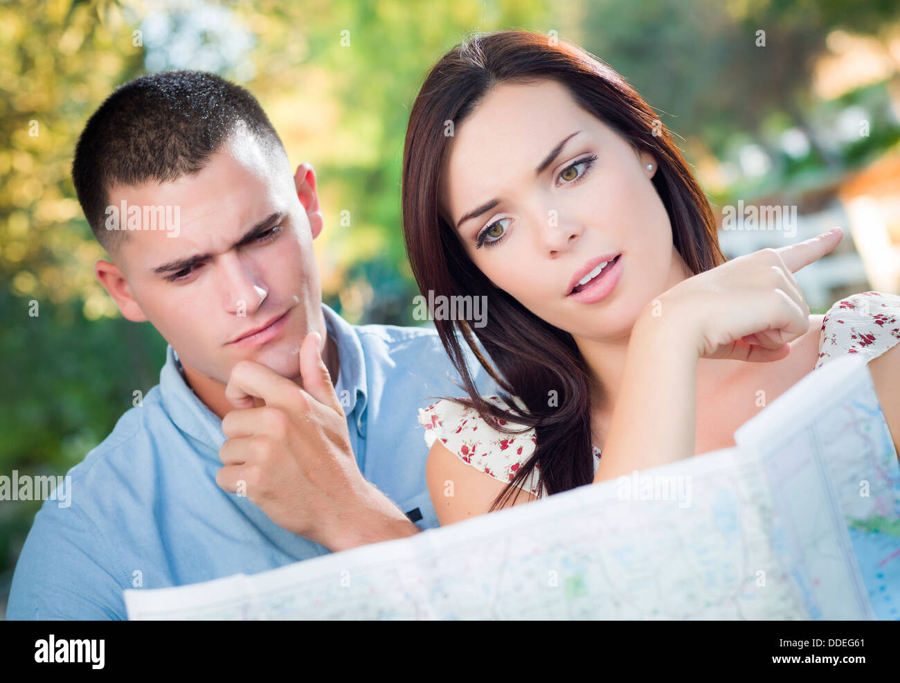 Lost and Confused Mixed Race Couple Looking Over A Map Outside Together. Stock Photo