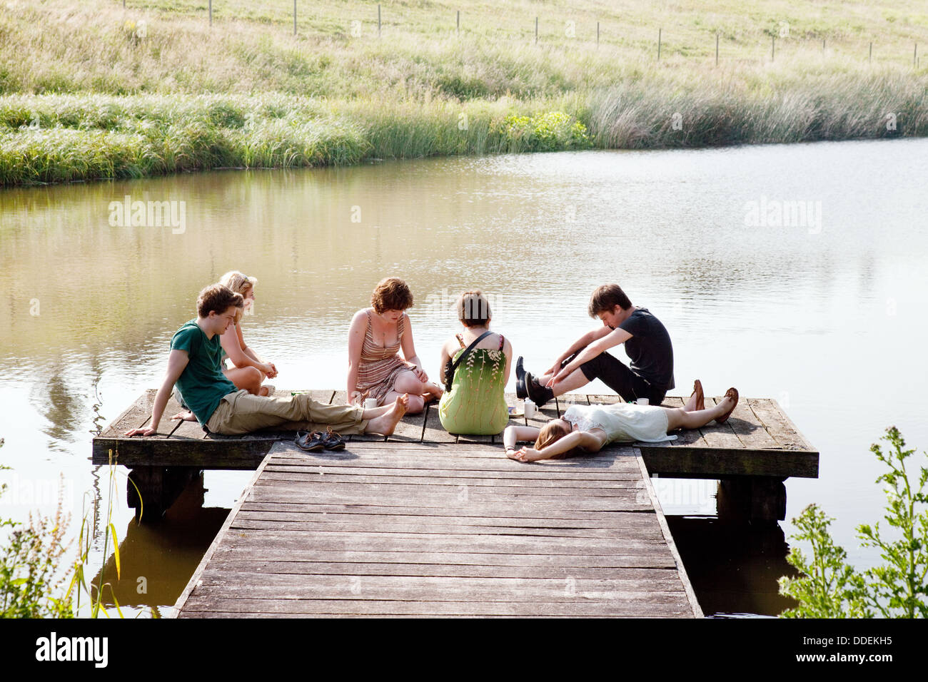 Summer people UK; A group of teenagers sitting on a jetty by a lake in summertime,  Lambourn, Berkshire England UK Stock Photo