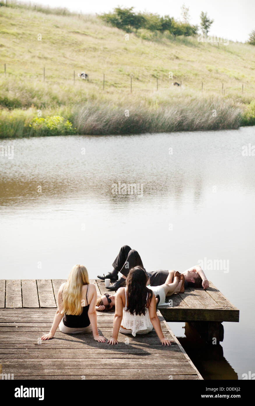 Teenagers sitting on a jetty by a lake in english countryside, Sheepdrove Organic Farm, Lambourn, Berkshire, UK Stock Photo