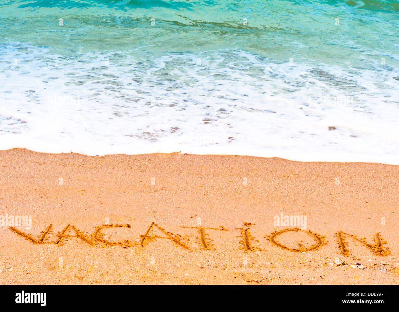 Vacation ; written in the sand on the beach blue waves in the background Stock Photo