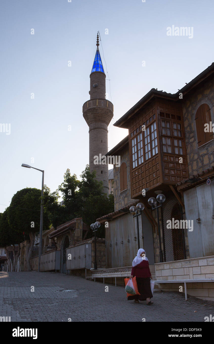 An elderly Turkish woman in traditional dress walks with her shopping past the mosque in Side, Turkey Stock Photo