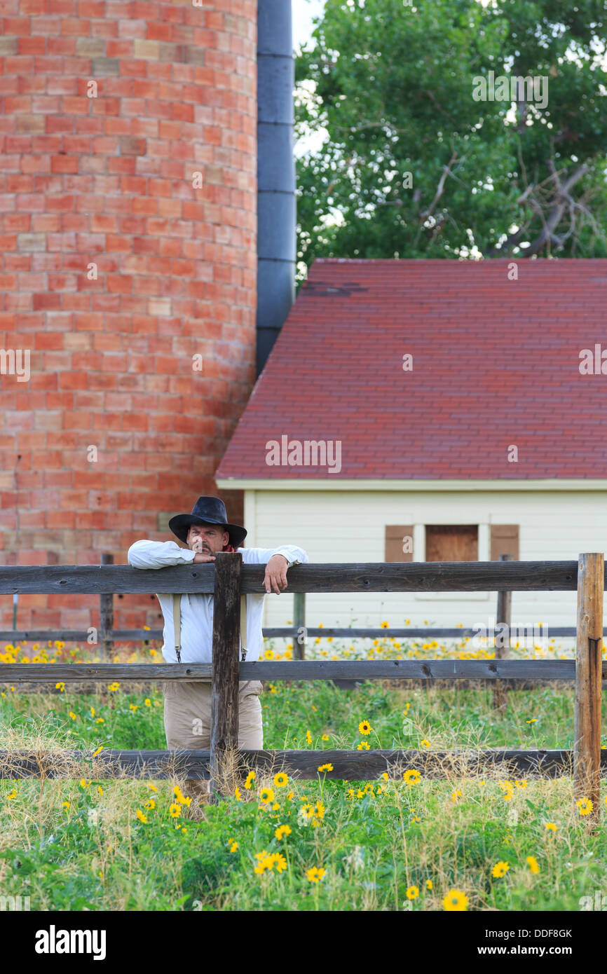 A cowboy rests against a corral fence and gazes into the distance Stock Photo