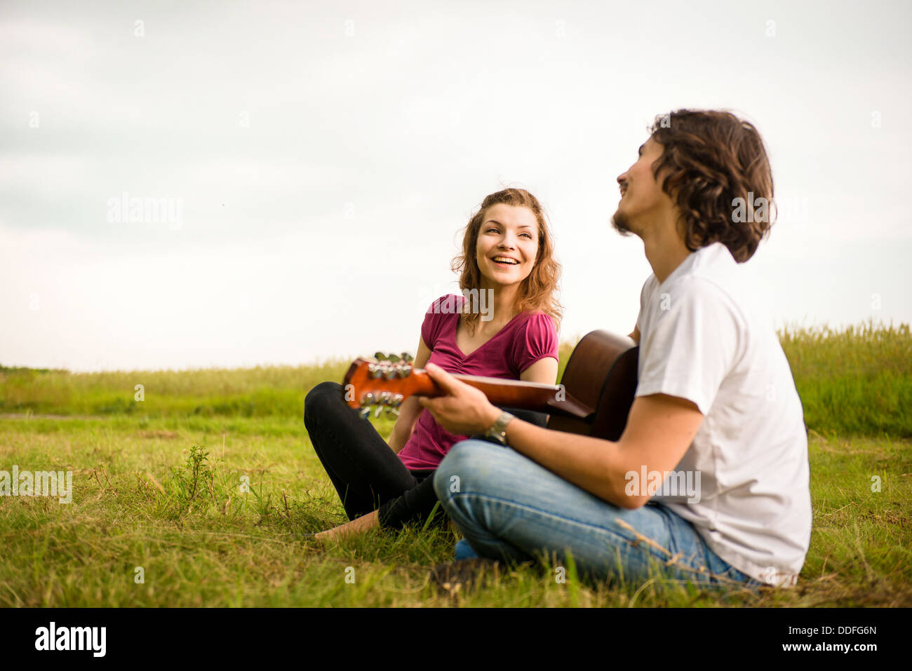 Young man playing to his girlfriend on guitar in nature - outdoor lifestyle Stock Photo