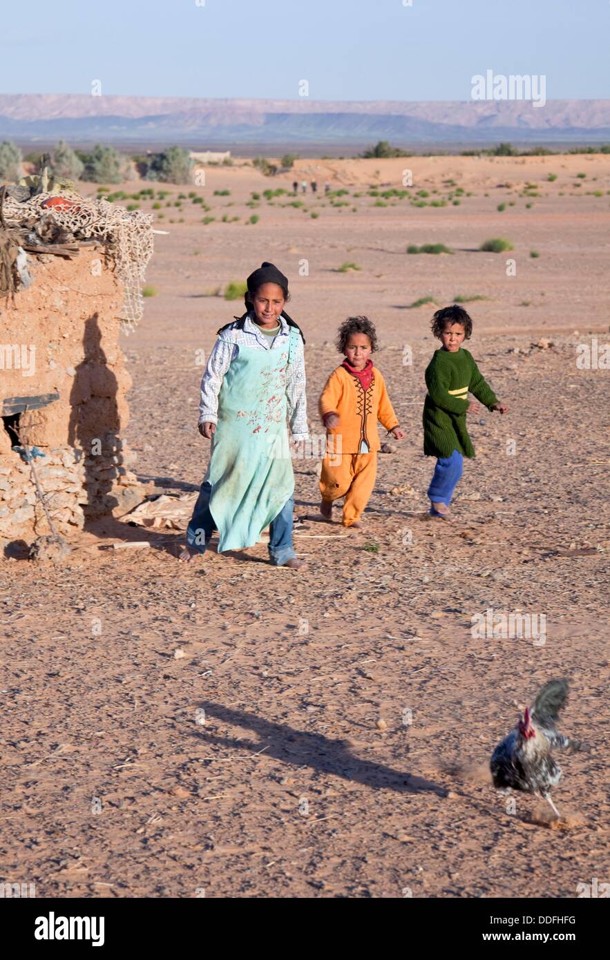 Morocco Erfoud Erg Chebbi Black Desert Village with local children chasing a chicken Stock Photo