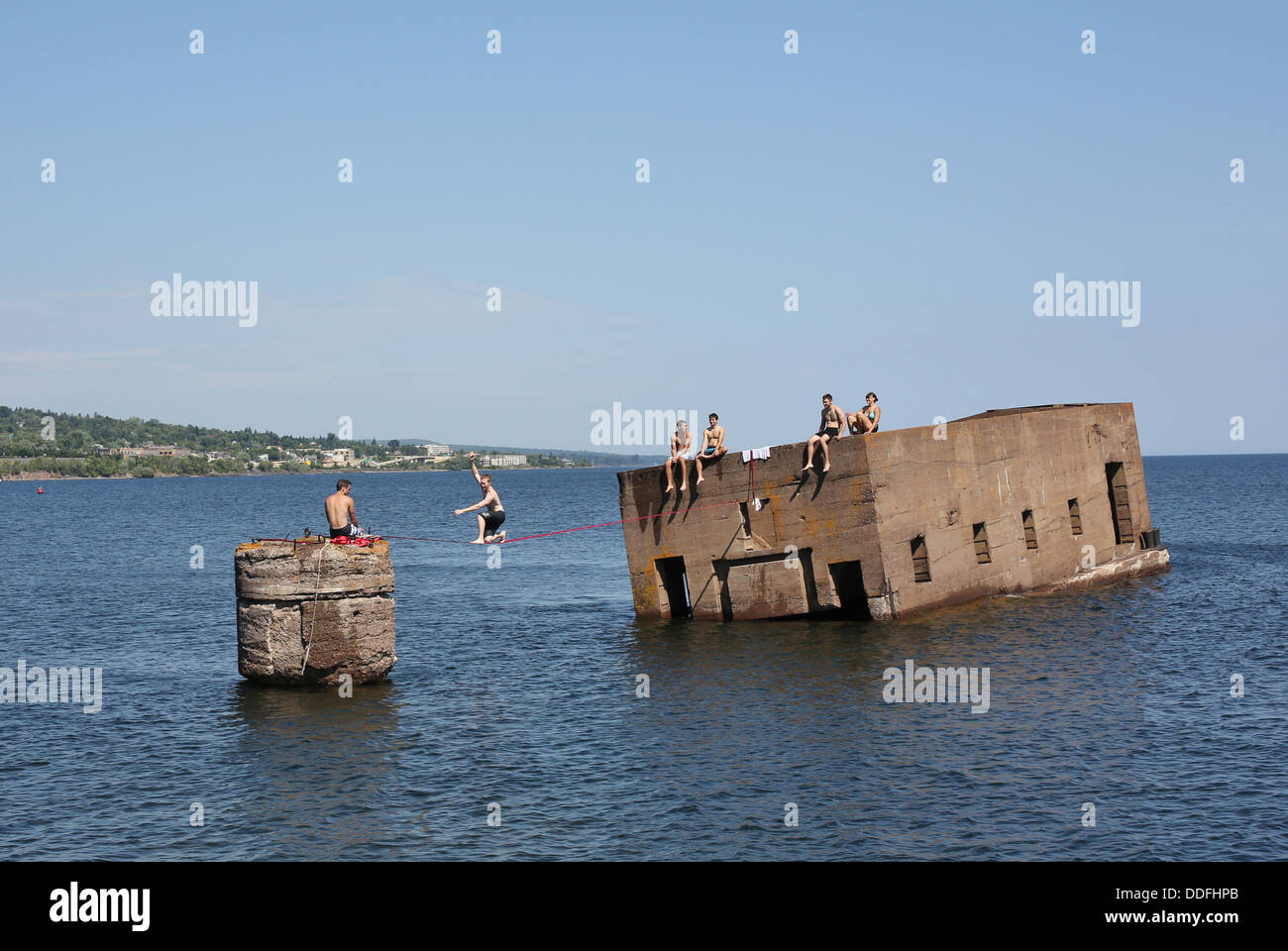 Teenagers walking a tightrope over water. Stock Photo