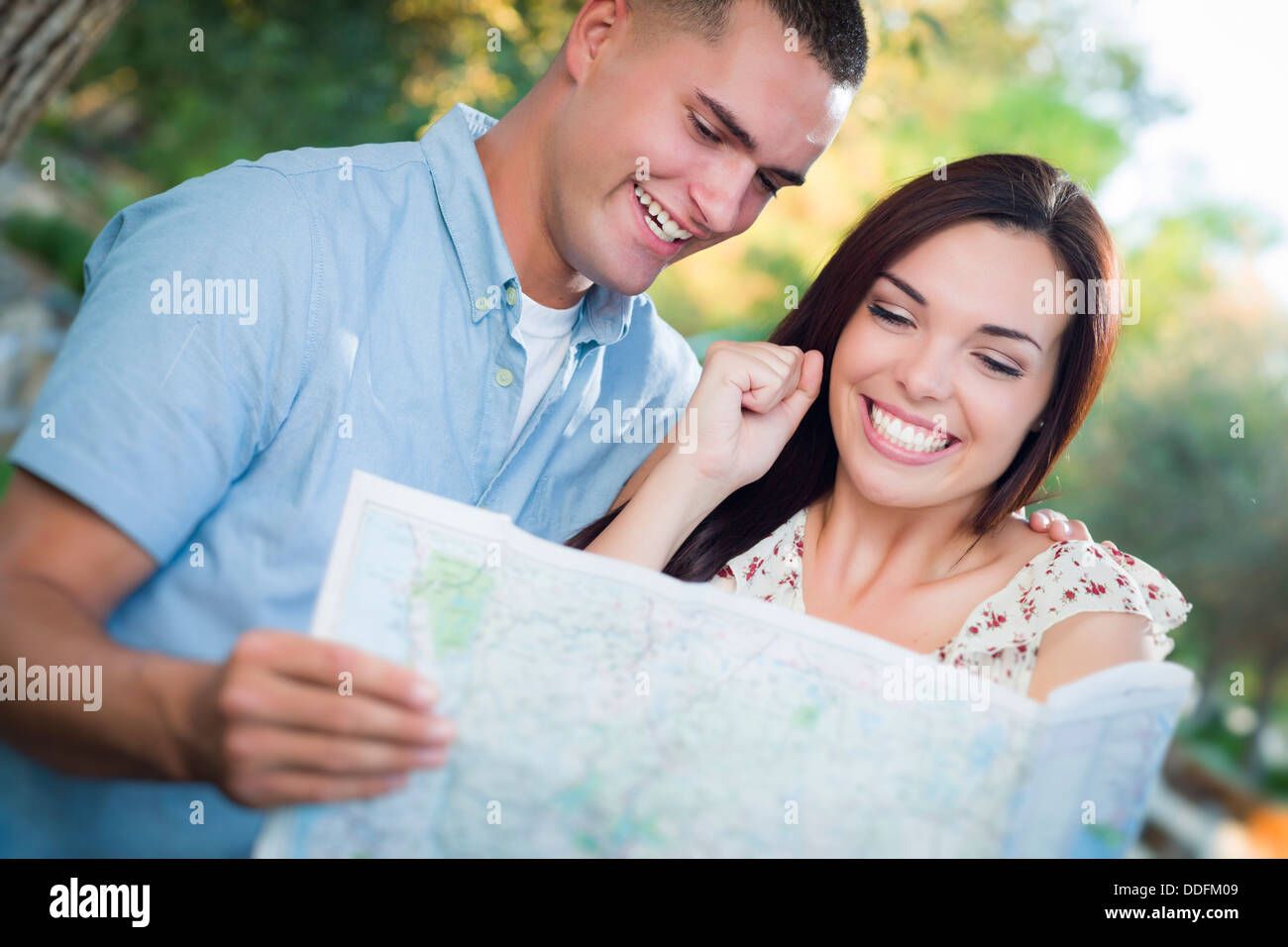 Happy Mixed Race Couple Looking Over A Map Outside Together. Stock Photo