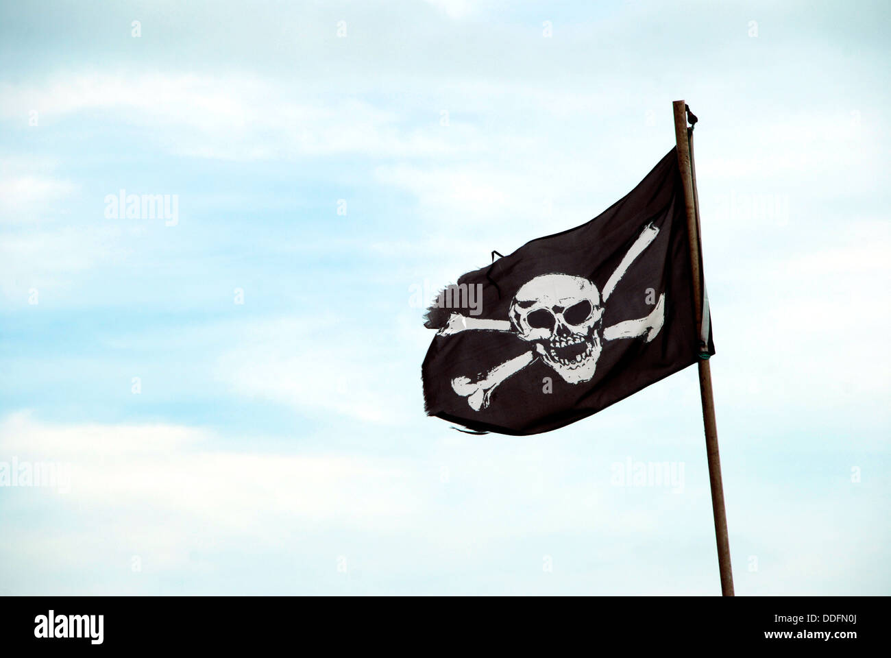 Ragged pirate flag with skull and crossbones flying from flagpole Stock Photo Alamy