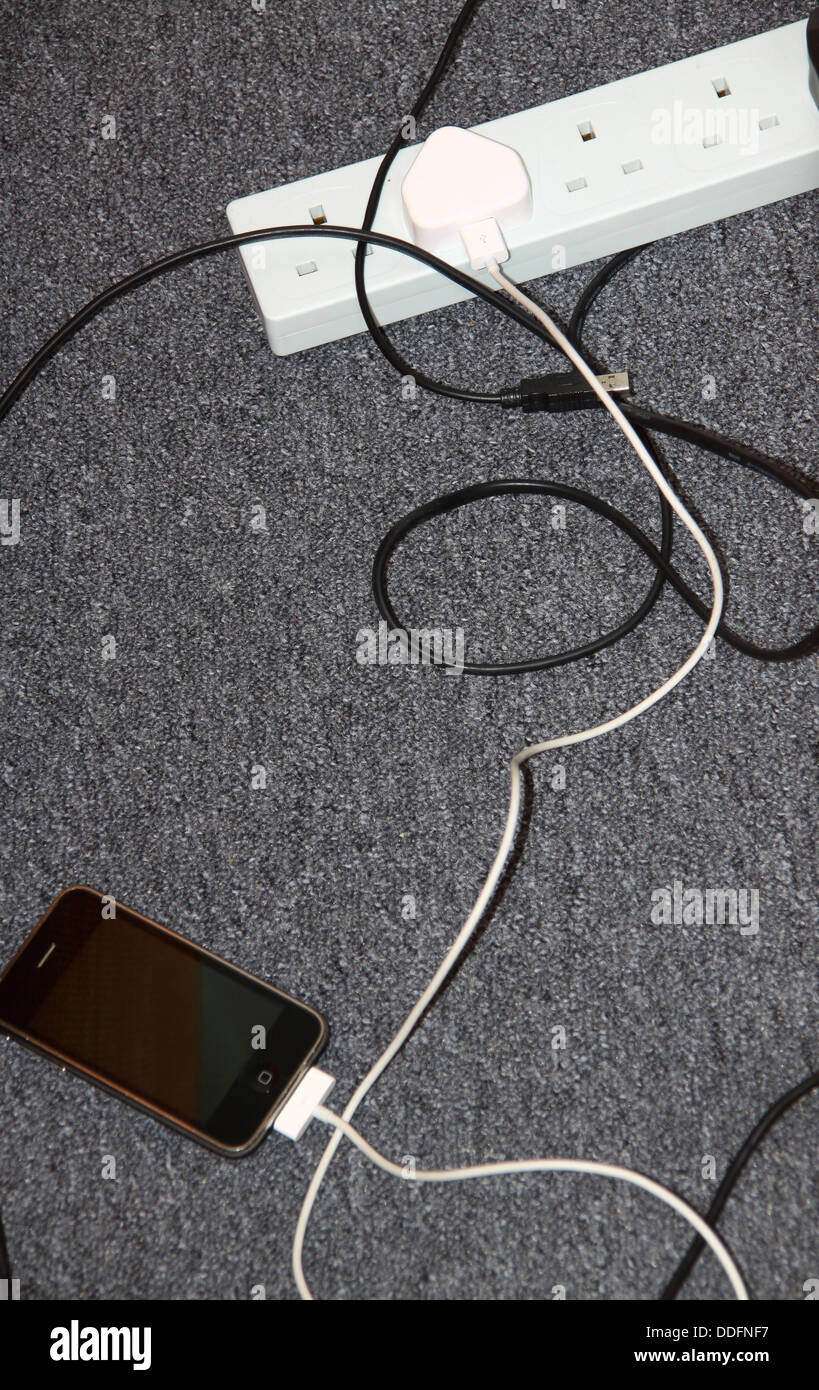 iPhone charging plugged into extension socket on floor Stock Photo