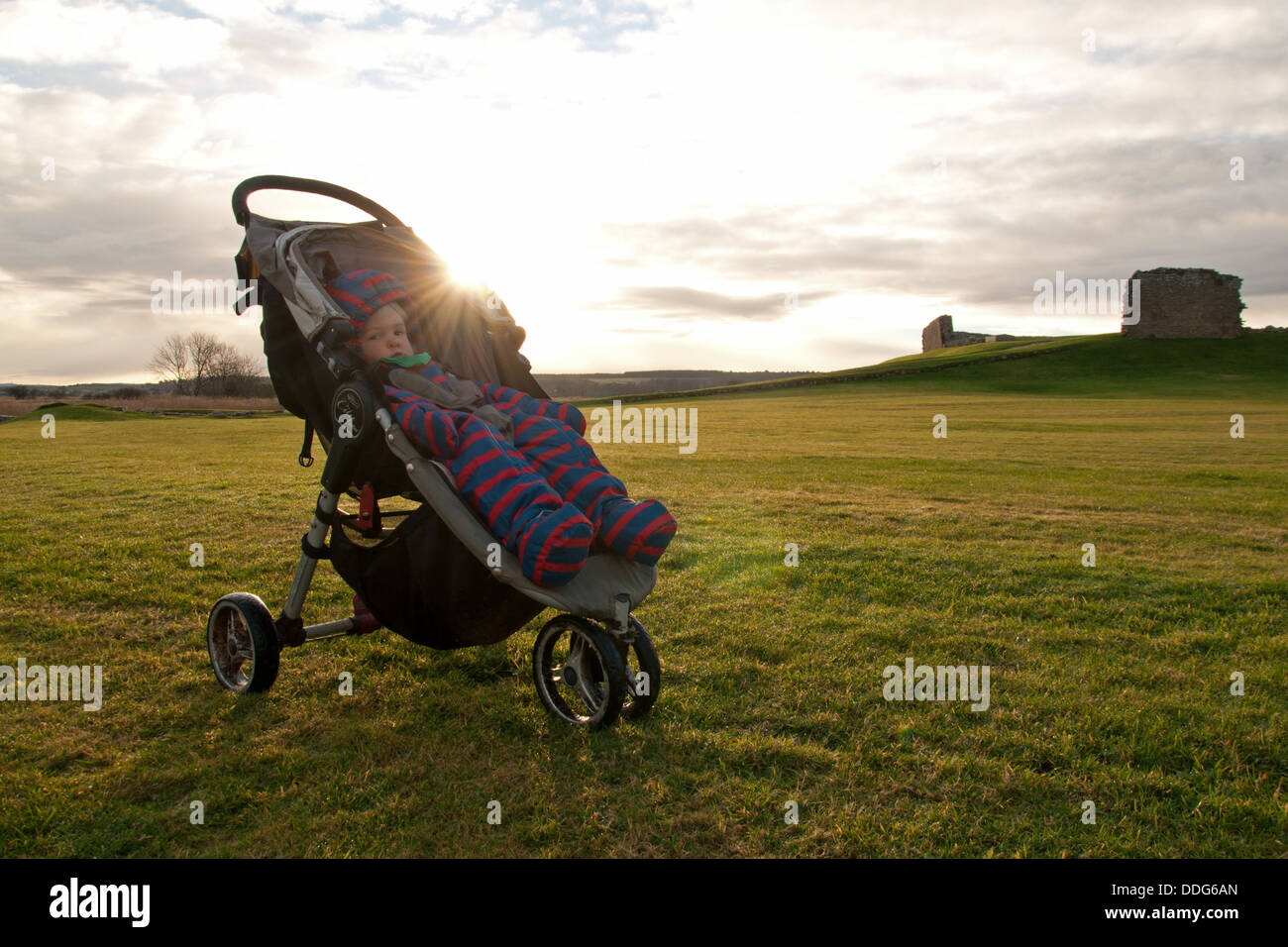 Baby in buggy wearing snowsuit with sun behind in the grounds of Duffus Castle, Moray, Northern Scotland Stock Photo