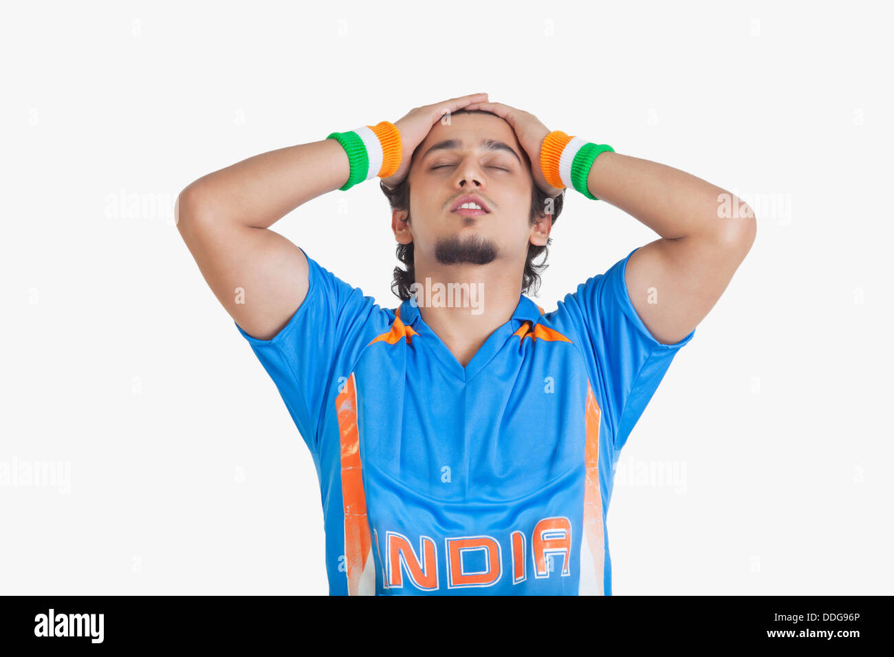 Displeased young man in Indian cricket team jersey standing with hands on head over white background Stock Photo