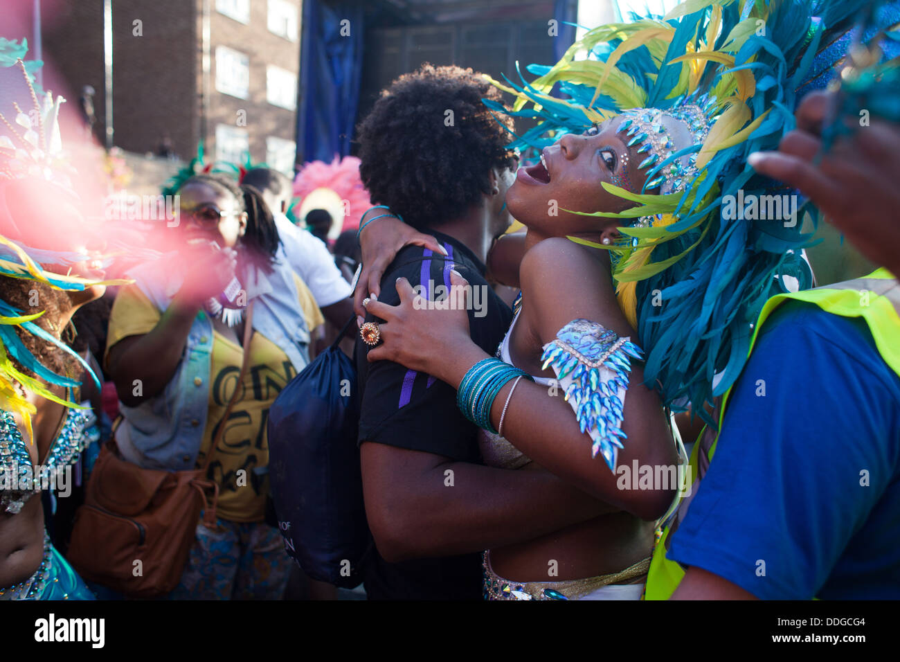 A black dancer dressed in colorful feather outfit and a skimpy bikini dance with a passing by man in the dying sunlight. Stock Photo