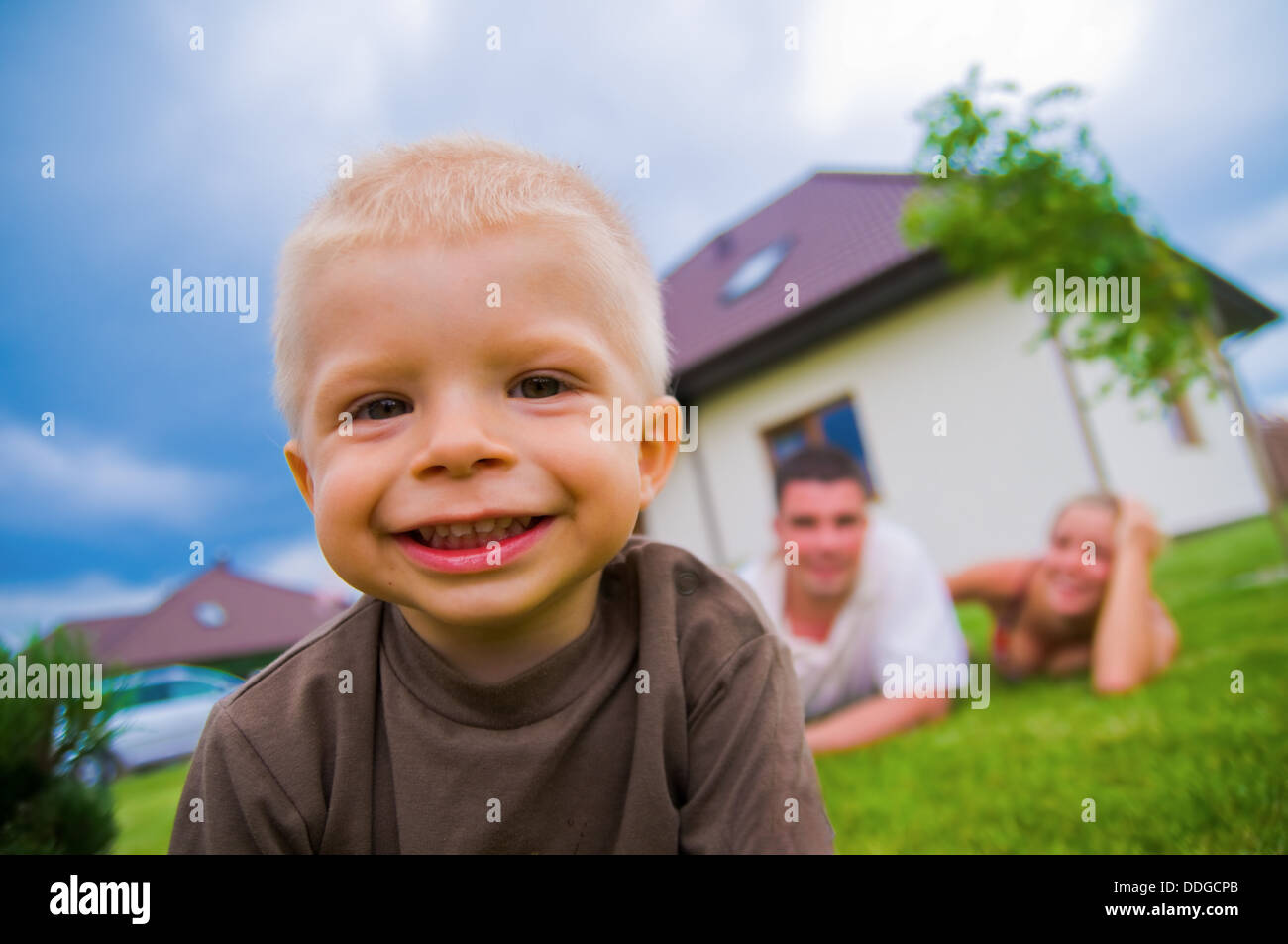 Happy child, in front of a house with parents in the background Stock Photo