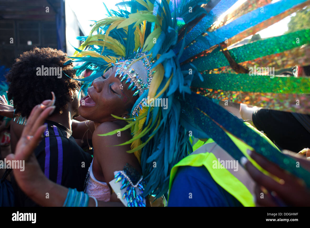 A black dancer dressed in colorful feather outfit and a skimpy bikini dance between two men in the dying sunlight. Stock Photo