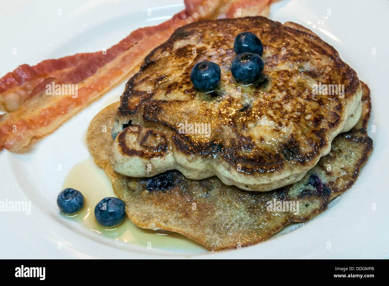 Two large blueberry pancakes topped with blueberries, maple syrup plus two strips of bacon. Stock Photo