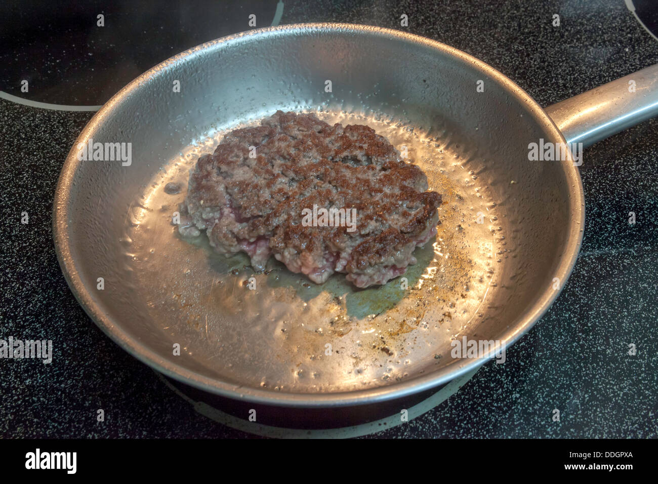 Greasy ground chuck hamburger patty frying in a small stainless steel