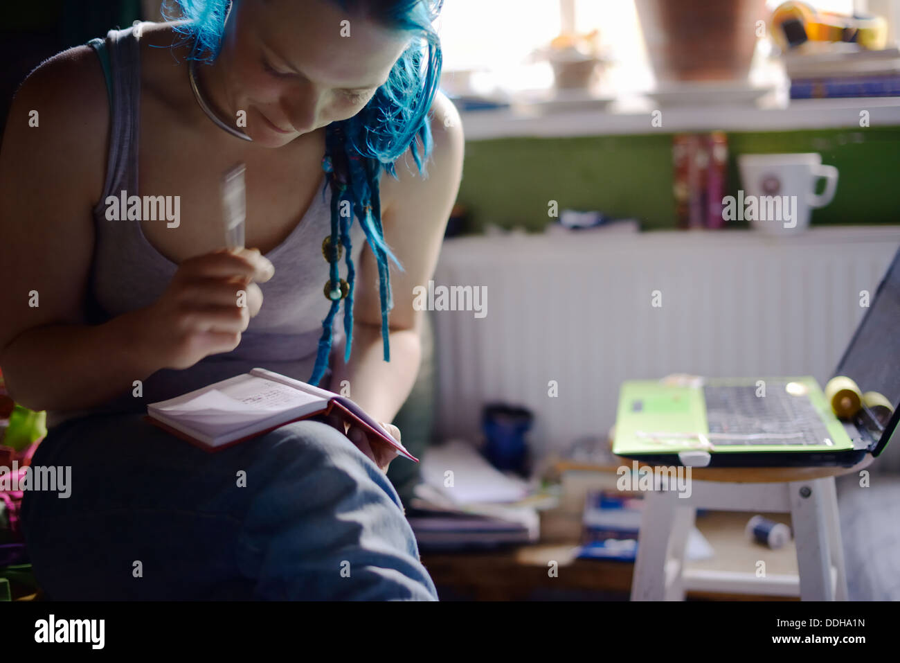 Young self employed businesswoman making notes in a notebook with laptop computer working at home, Wales, UK. Stock Photo