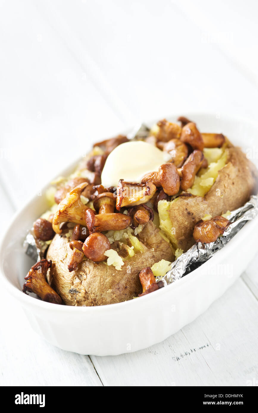 Baked potato with fried chanterelles and butter on rustic wooden