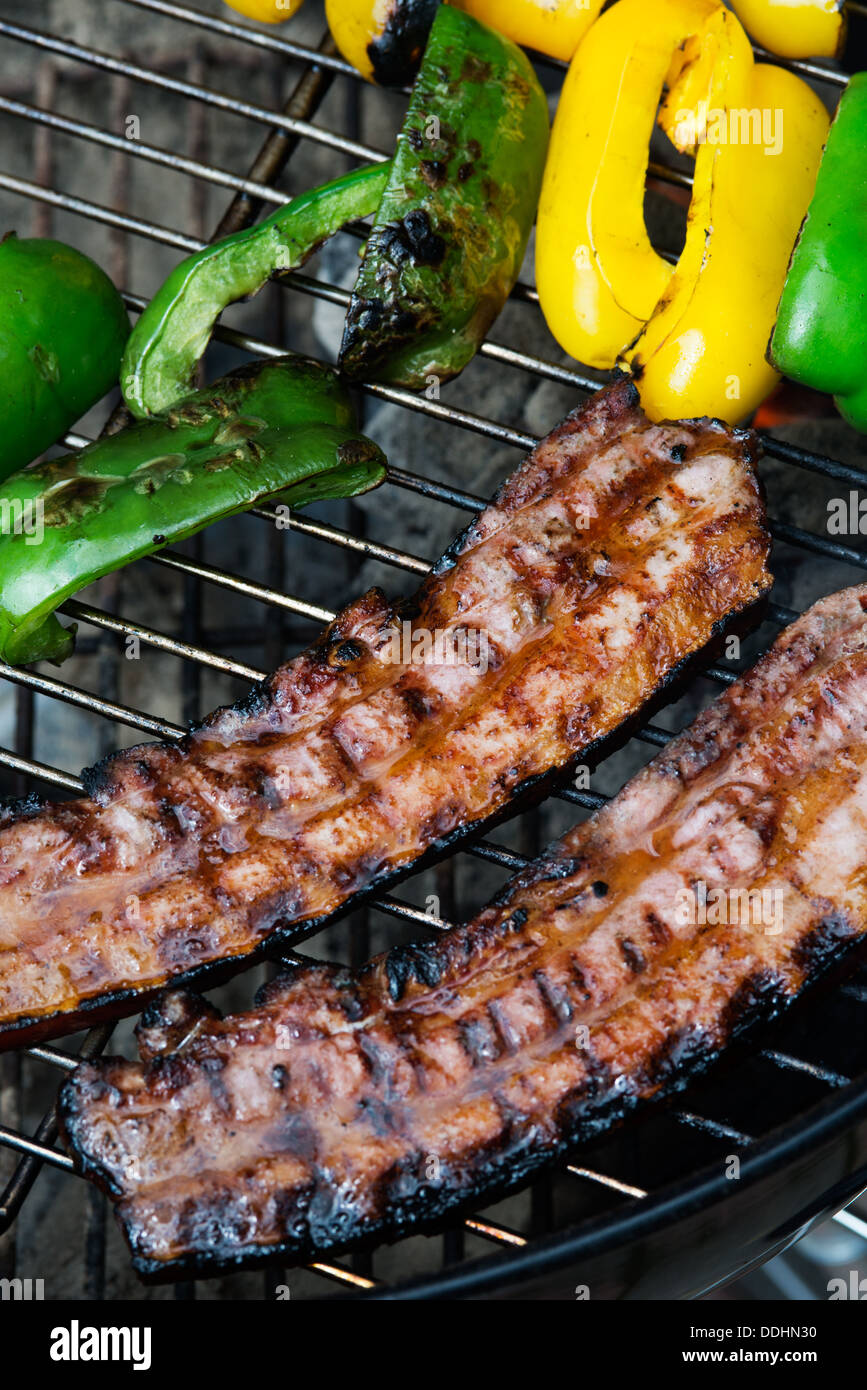 Two thick pieces of bacon on grill with yellow and green bell peppers Stock Photo