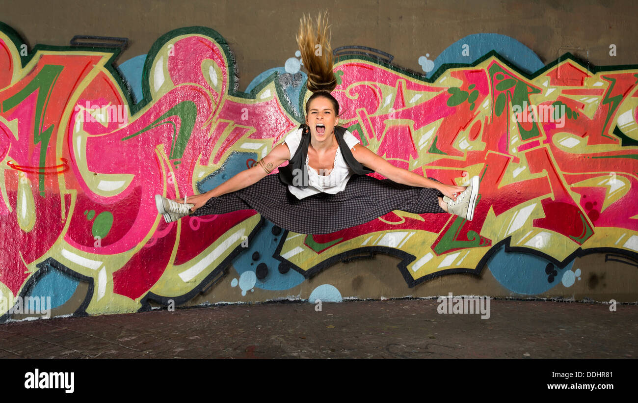 Hip-hop dancer jumping in front of a wall with graffiti Stock Photo