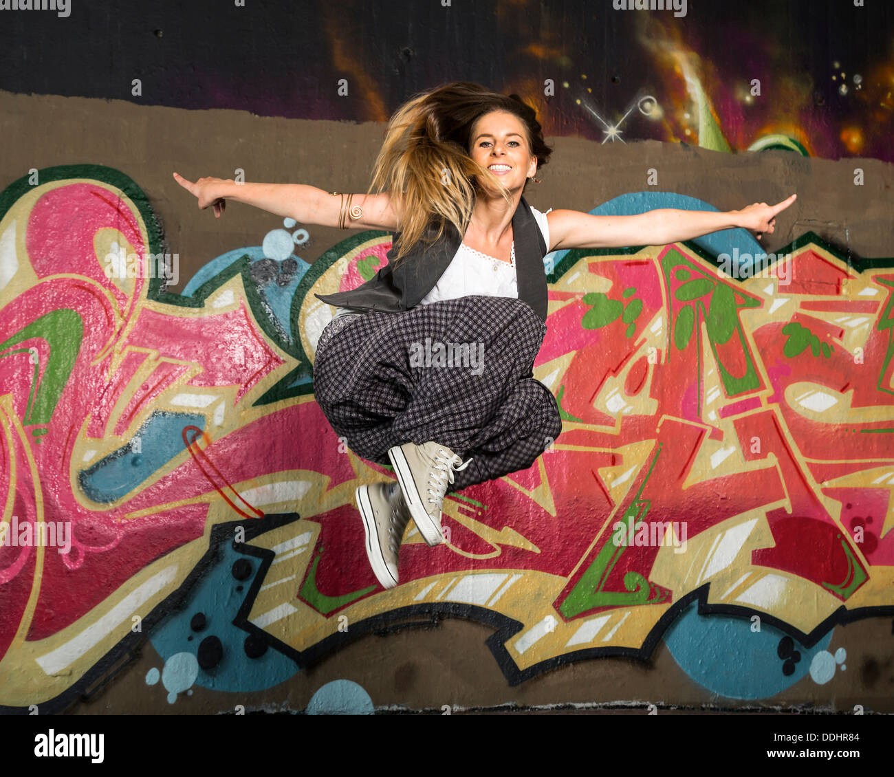 Hip-hop dancer jumping in front of a wall with graffiti Stock Photo