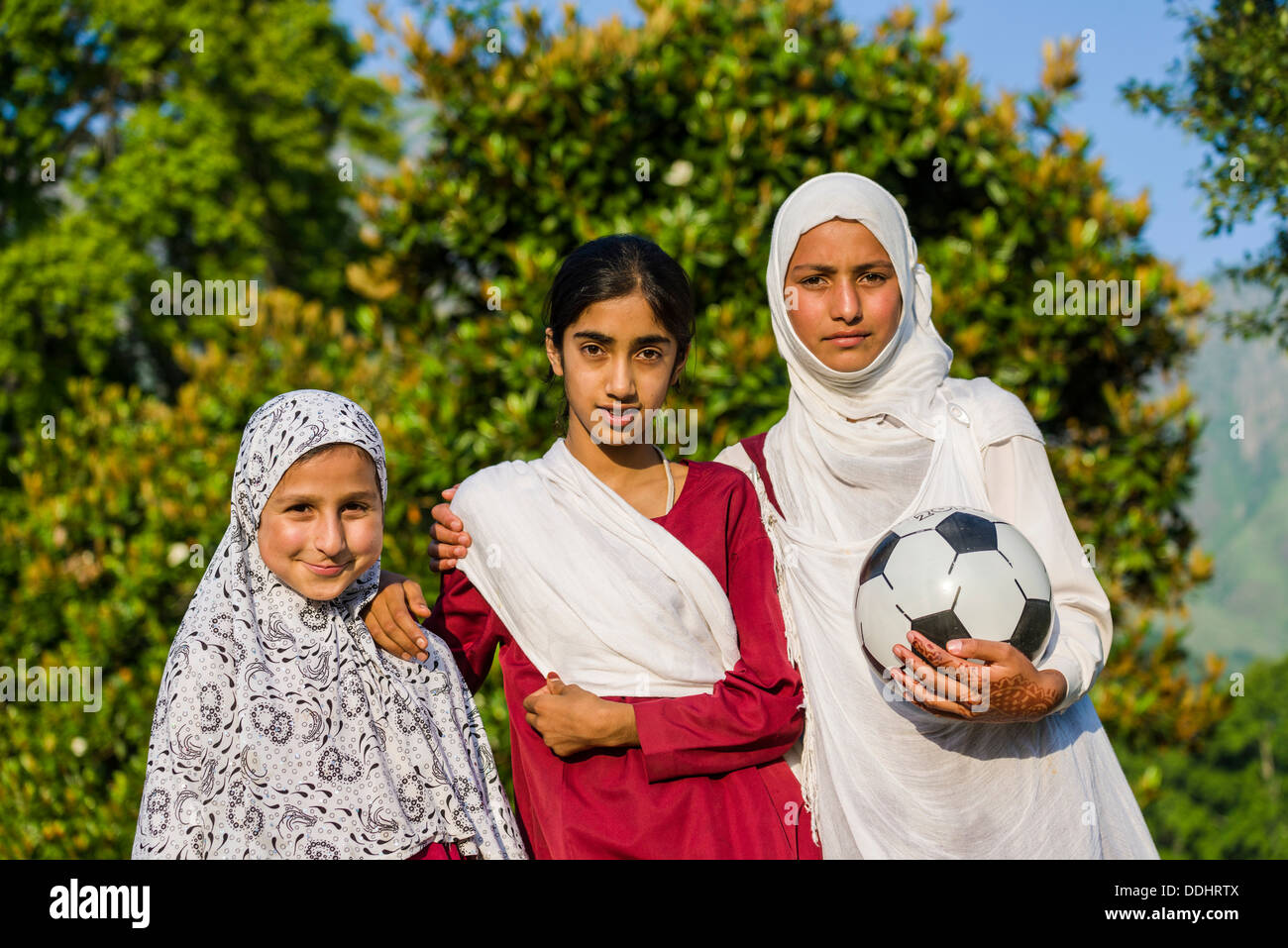 Three Kashmiri girls, one holding a soccer ball, two wearing headscarves Stock Photo