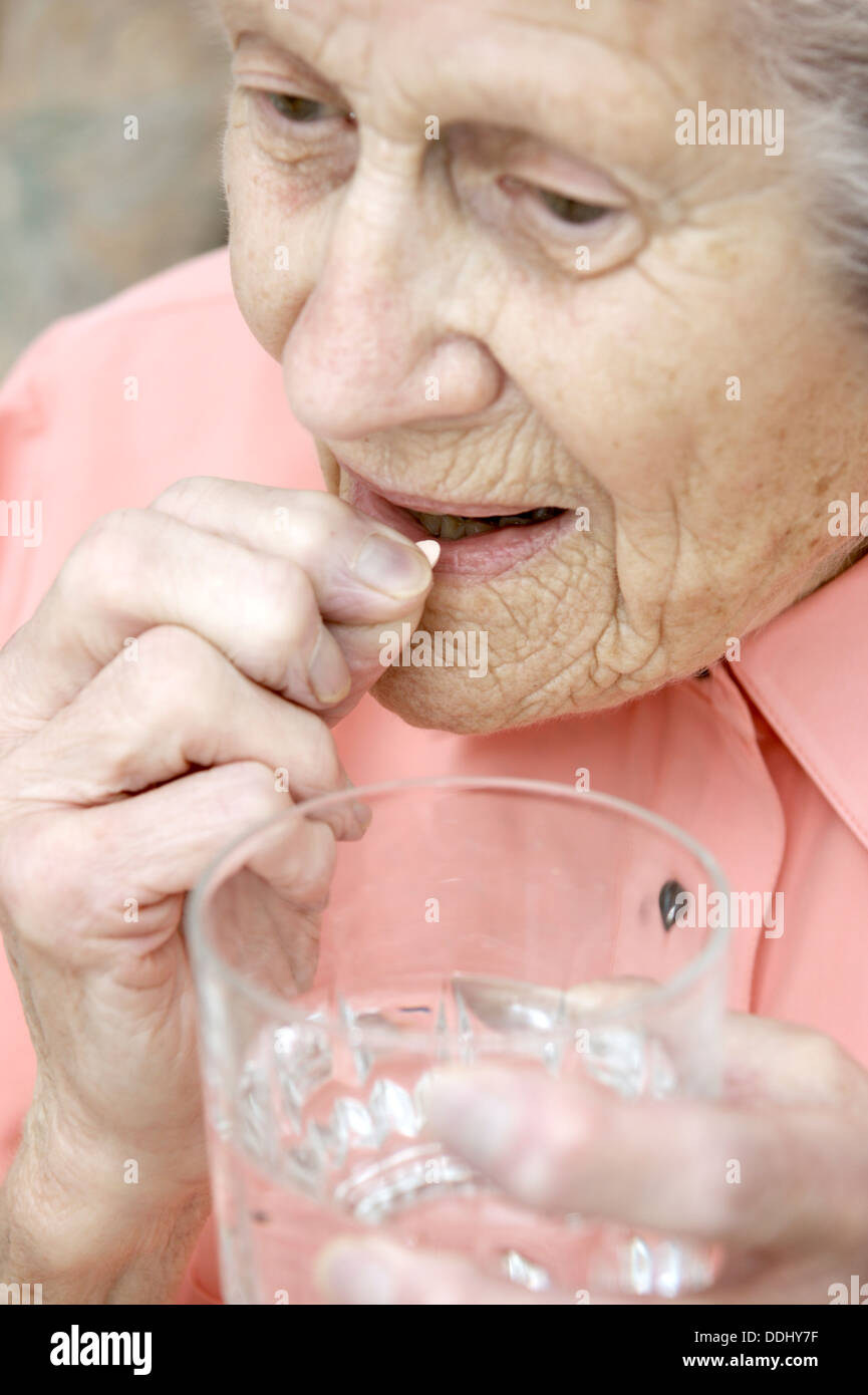 Elderly woman taking a Simvastatin tablet (statins) drugs that reduces the amount of cholesterol & triglycerides in the body Stock Photo