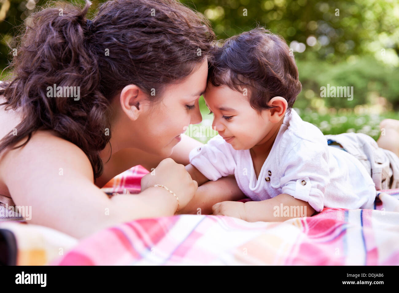 Mother cuddling her baby boy on blanket, smiling Stock Photo