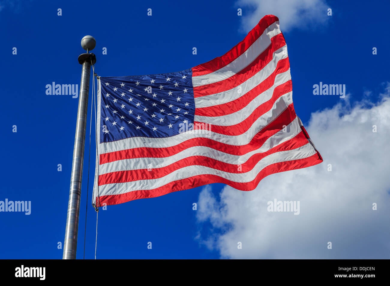 A photograph of an American flag blowing in the breeze against a very blue sky with some contrasting clouds Stock Photo