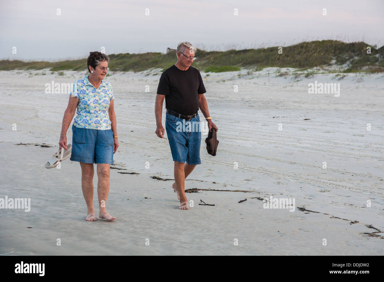 Senior man and woman carry shoes while walking and looking for shells on beach at Daytona Beach, Florida Stock Photo