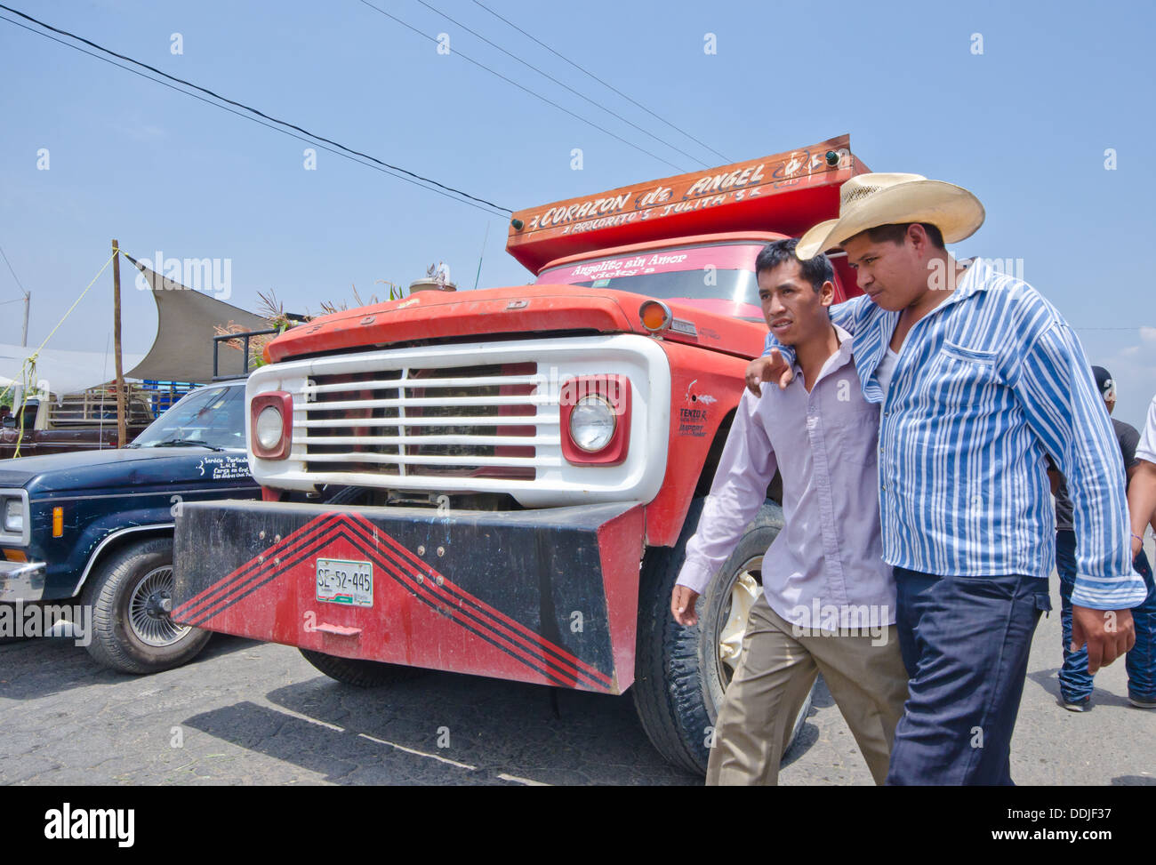 Two male friends, one with arm around the other, walking on road in front of truck in Mexico Stock Photo