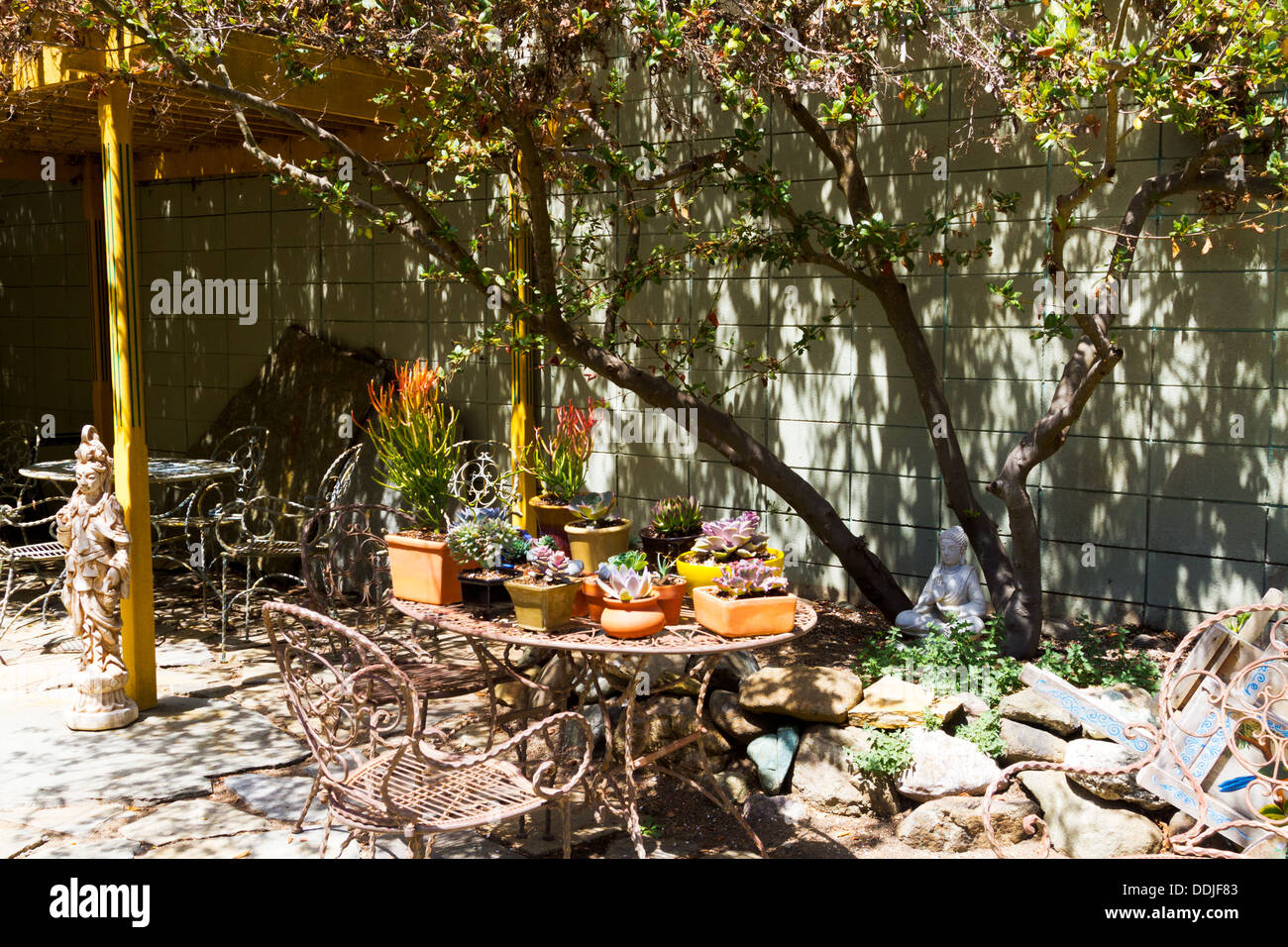 Succulents and wrought iron furniture display on a sunlit patio with interesting shadows. Stock Photo