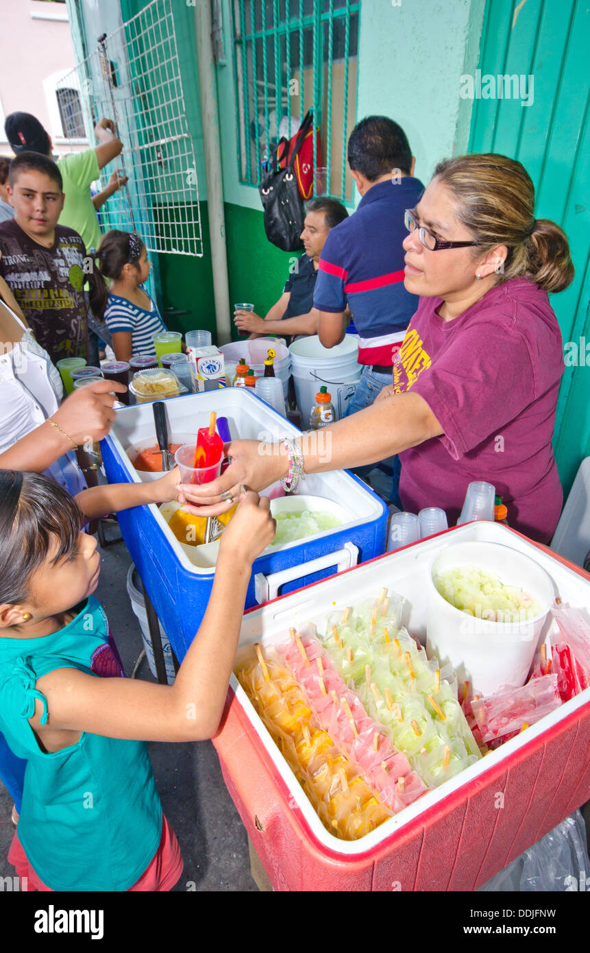 A woman sells ice lollies in a food festival in Puebla city.  A child is receiving her ice whilst people queue behind. Stock Photo
